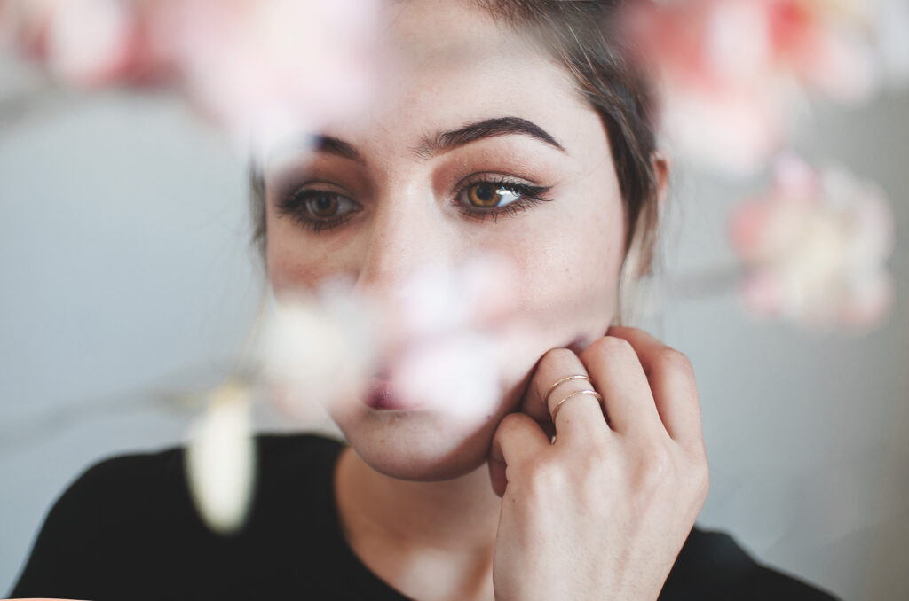 Darian Rojas's portrait captures a serene moment with soft pink flowers framing her face her gaze directed to the side and a delicate ring on her finger.